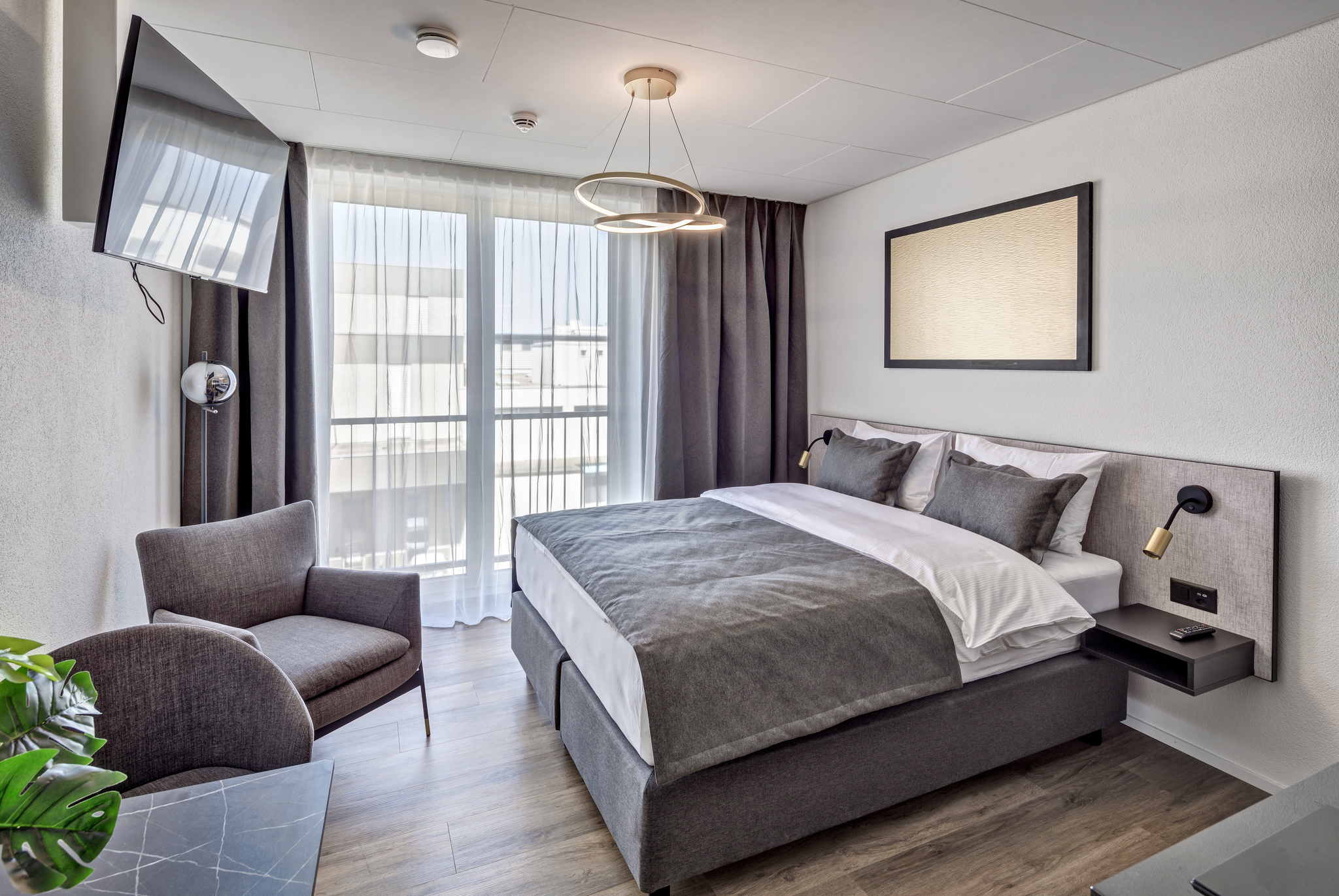 Aufnahme eines Schlafzimmers der Serviced Apartments in der Schweiz mit großem Bett, TV und Sessel vor einer hellen Fensterfront